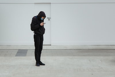 身穿黑色连帽衫和黑色裤子的男子站在白墙附近